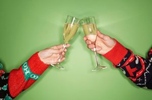 two people in Christmas jumpers clinking Champagne flutes