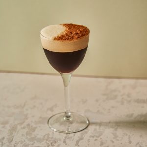 A brown cocktail with foam on a table
