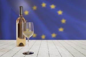 EU flag with bottle and glass of white wine on wooden surface