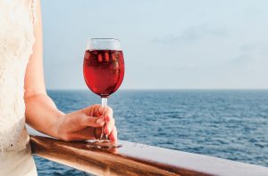 Hand holding glass of red wine with chill, overlooking the sea
