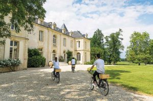 Three people on bicycles approaching Château de Reignac in Entre-deux-Mers