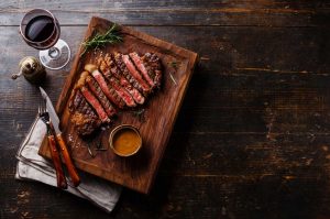 Steak and pepperorn sauce o a wooden board with red wine