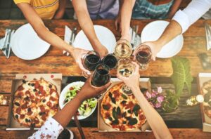 People clinking wine glasses above table with pizza