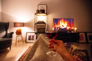 Person wrapped in blanket on sofa with glass of red wine