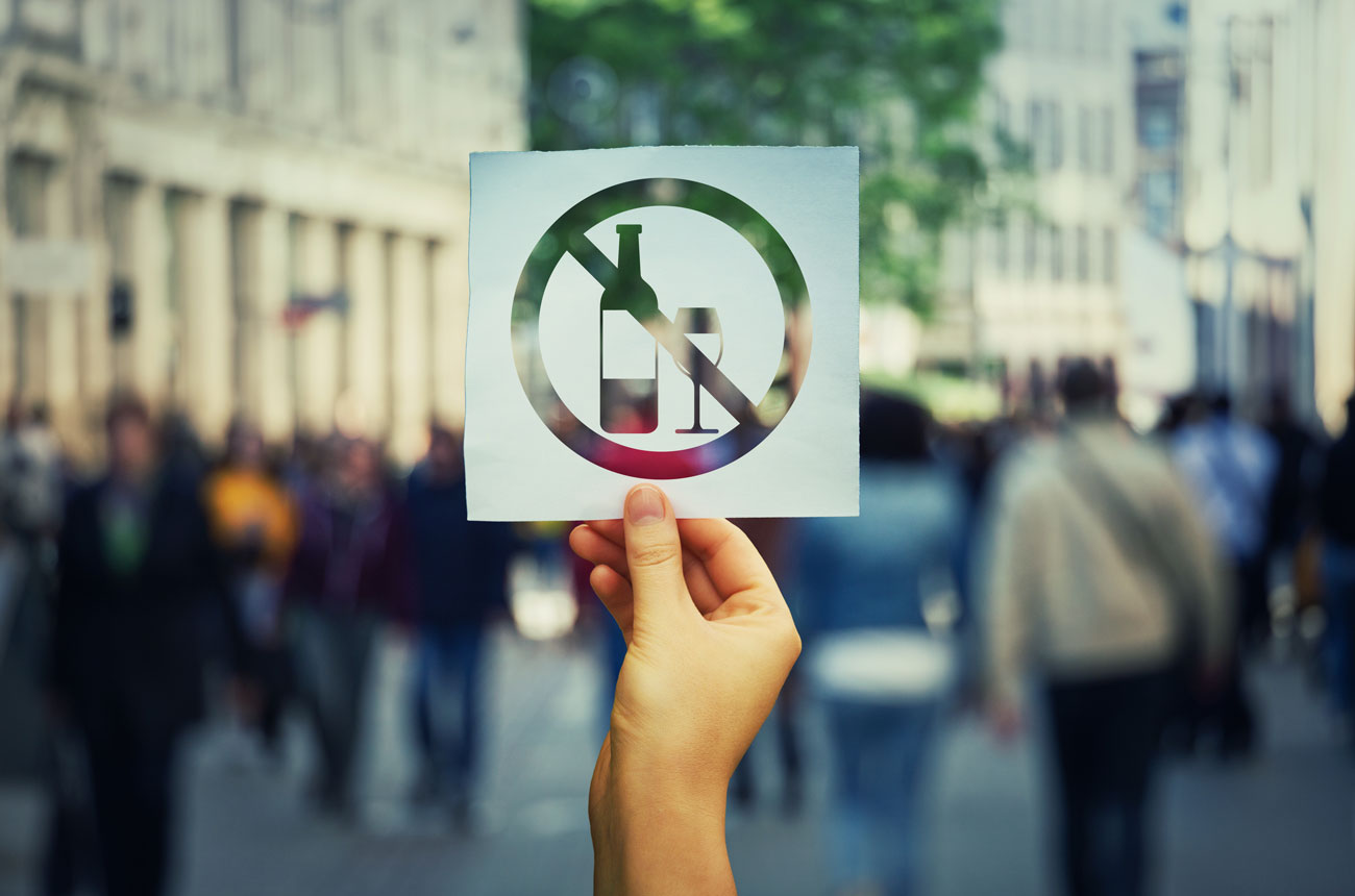 Hand holding sign with no alcohol symbol in outdoor setting