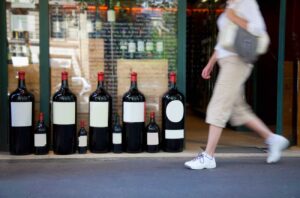 Woman walking past shop with large wine format bottles in window